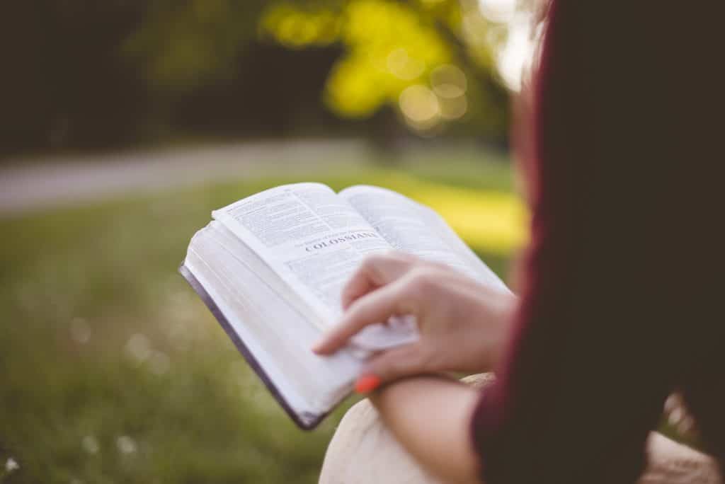 A closeup shot of a female sitting while reading the bible with a blurred background