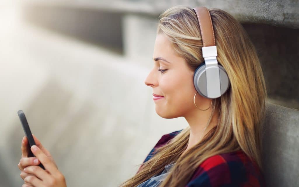 an attractive young woman leaning against a wall and listening to music while using her cellphone